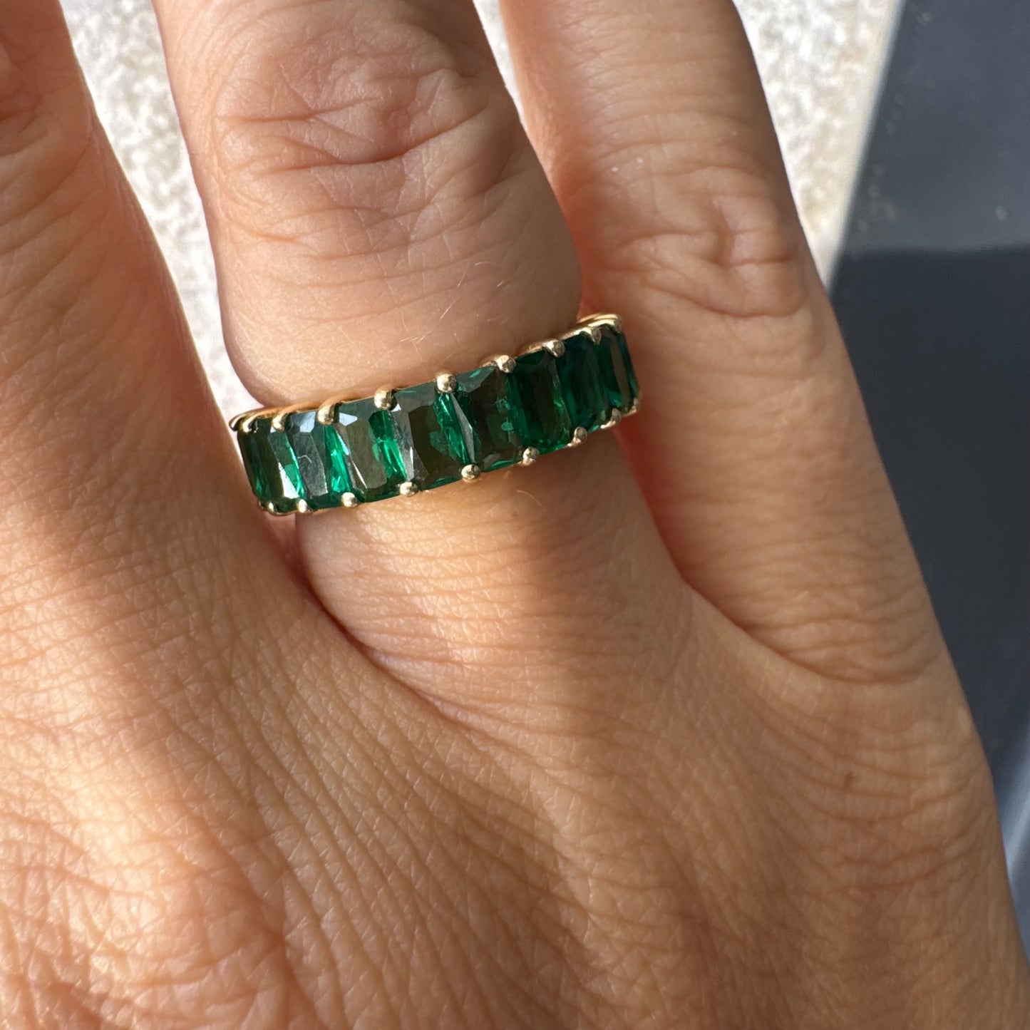 טבעת זהב צהוב 14 קראט משובצת אבנים ירוקות בחיתוך אמרלד, בעיצוב חצי איטרניטי.