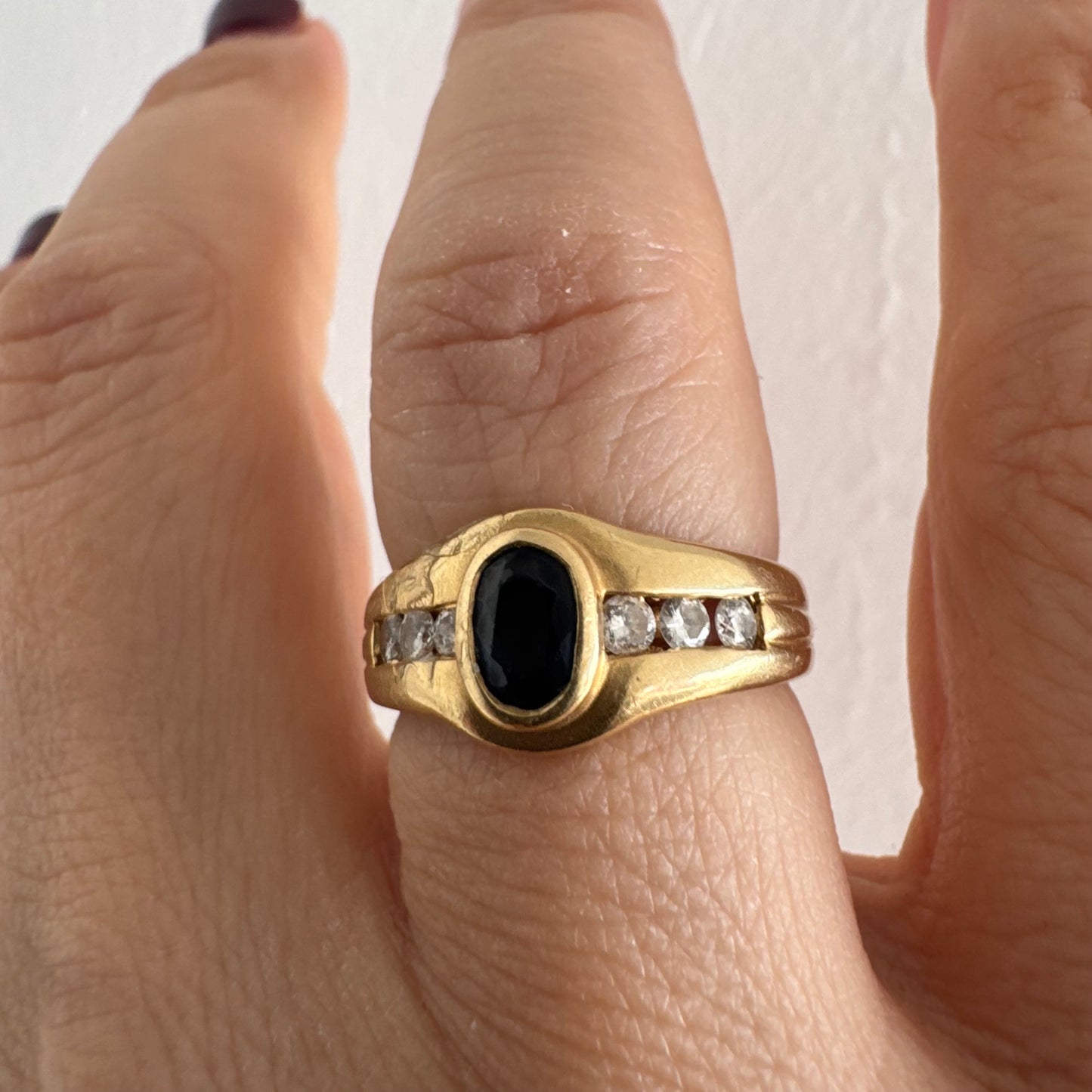 טבעת זהב צהוב 18 קראט משובצת אבן ספיר אובלית בגוון כחול עמוק, במסגרת חלקה ומודגשת, ומשני צדדיה שורת יהלומים משובצים בתעלה.