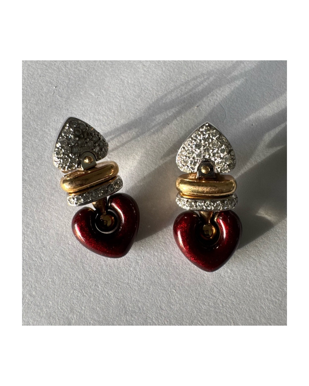 עגילי זהב 18 קראט בשילוב זהב צהוב ולבן, משובצים יהלומים בחלק העליון ובחישוק מרכזי, ובתחתית תליון לב אדום בגימור מבריק.