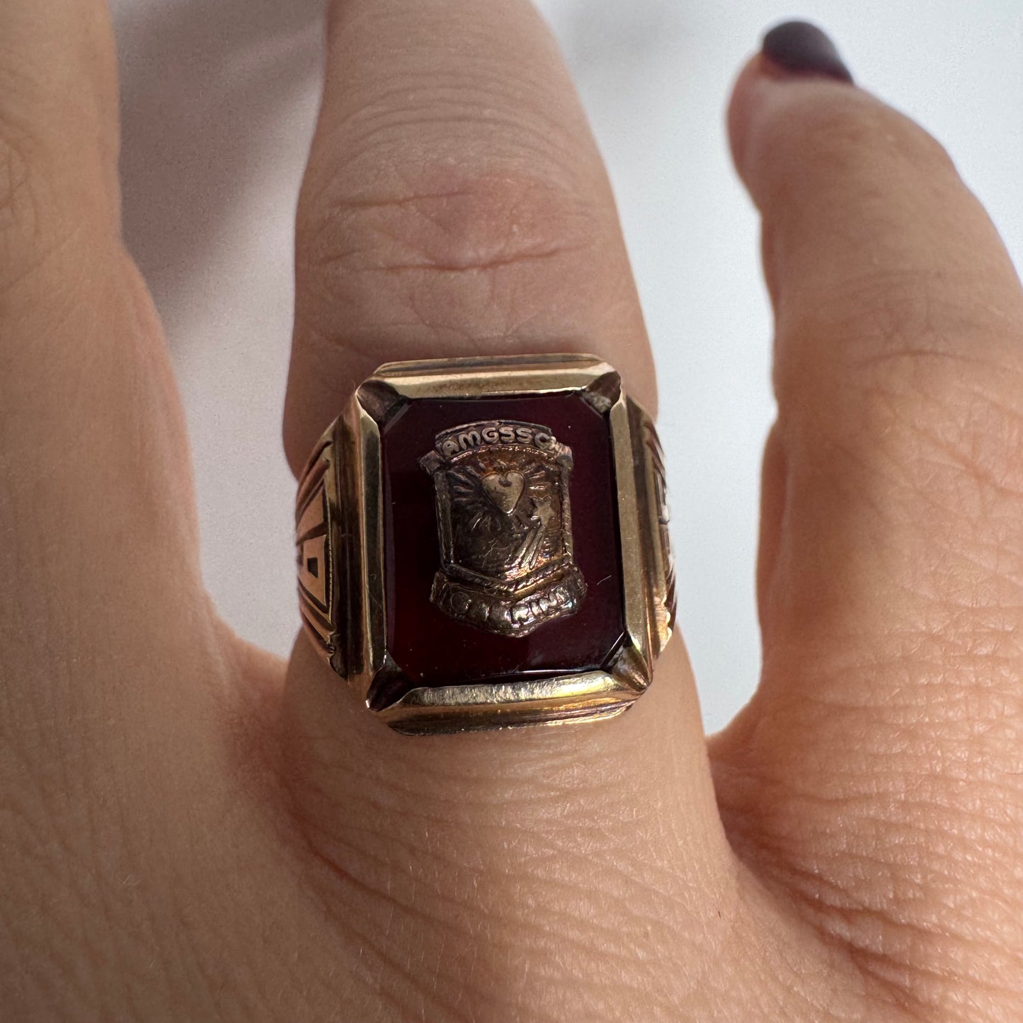 טבעת חותם זהב 10 קראט עם לוח מרכזי בגוון בורדו עמוק ועיטור סמל מובלט.
