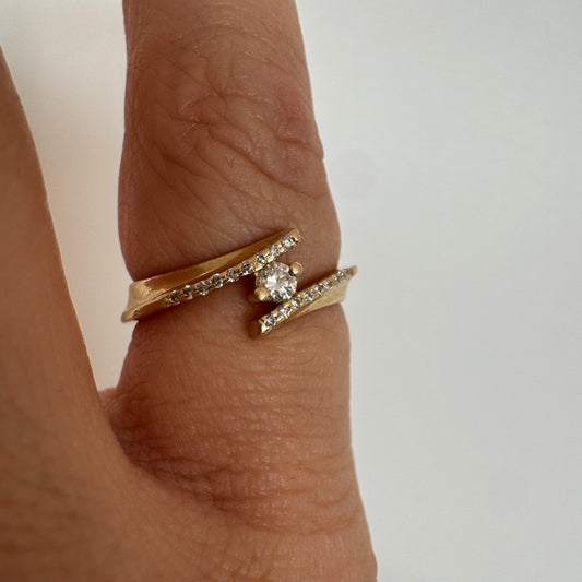 טבעת זהב 14 קראט בעיצוב פתוח ואלגנטי, משובצת יהלום מרכזי ויהלומים עדינים לאורך הזרועות.