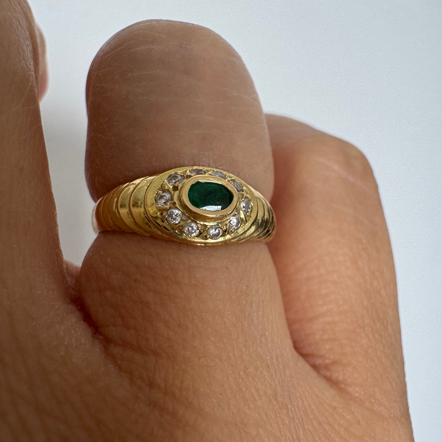 18K gold ring set with an oval Emerald at the center surrounded by Diamonds