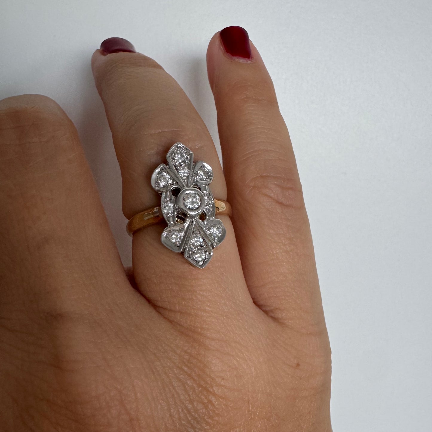 טבעת זהב לבן 14 קראט, בעיצוב אלגנטי ועדין, משובצת יהלום מרכזי עגול וסביבו יהלומים נוצצים נוספים.