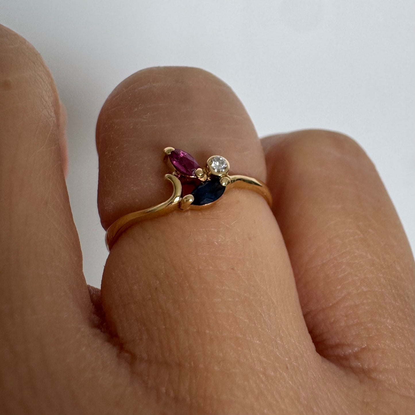 Delicate 18K gold ring set with pink and blue Sapphires alongside a sparkling center stone.