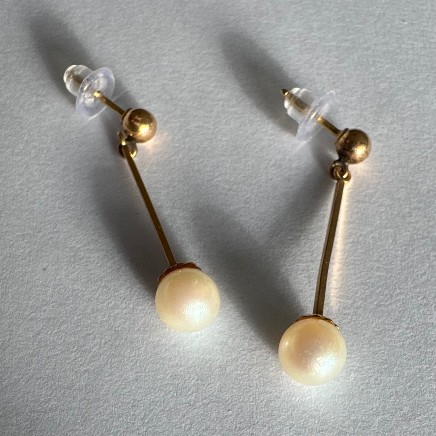 עגילי זהב 14 קראט בעיצוב תלוי ועדין, עם פנינה עגולה בקצה.