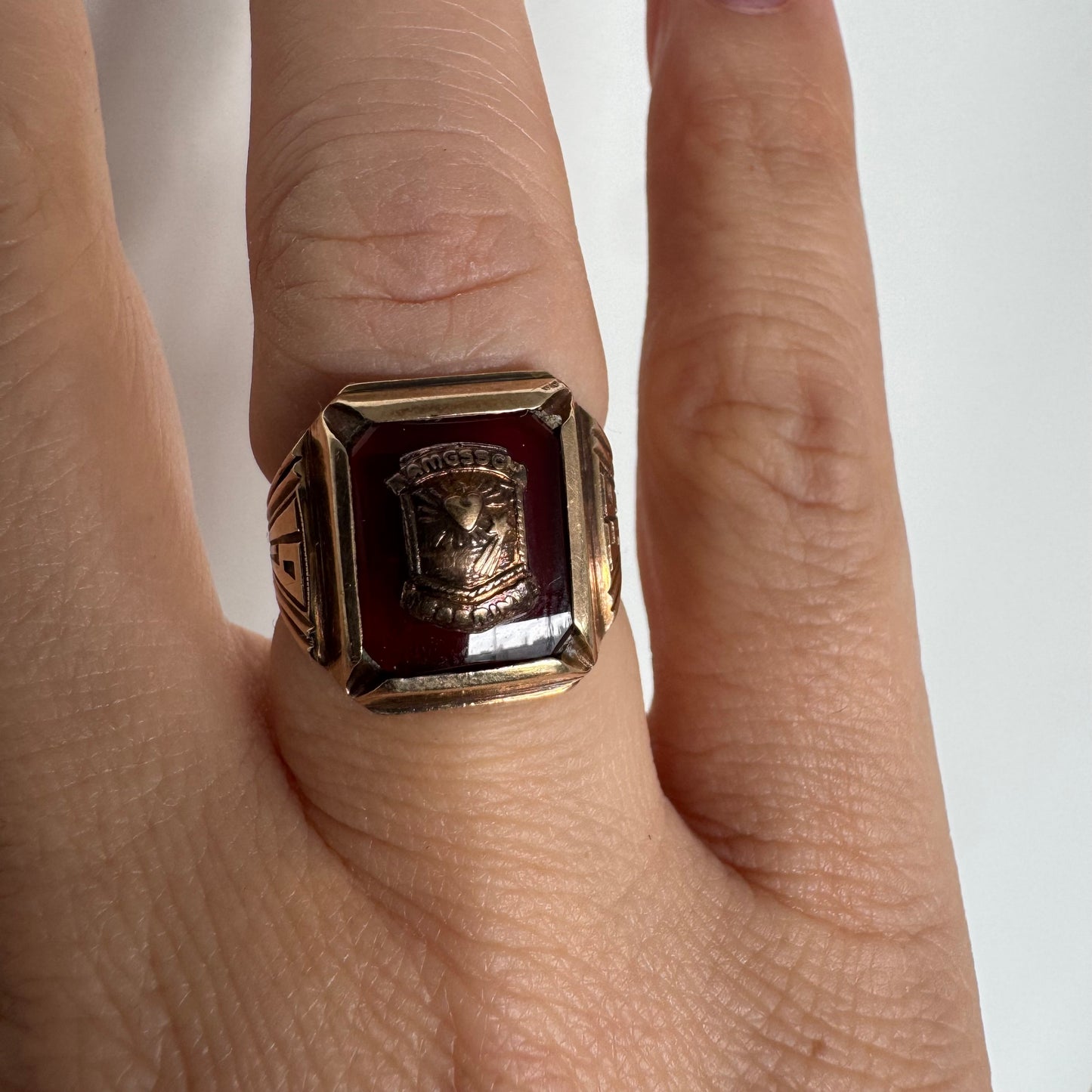 טבעת חותם זהב 10 קראט עם לוח מרכזי בגוון בורדו עמוק ועיטור סמל מובלט.