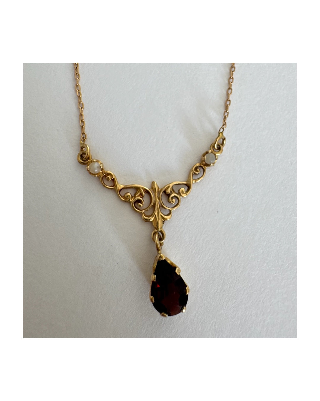 18K gold Necklace featuring an elegant scrollwork design and a striking deep-red pear-shaped Garnet drop.