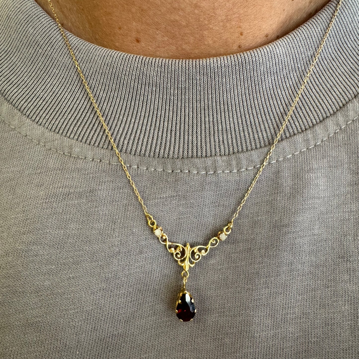 18K gold Necklace featuring an elegant scrollwork design and a striking deep-red pear-shaped Garnet drop.