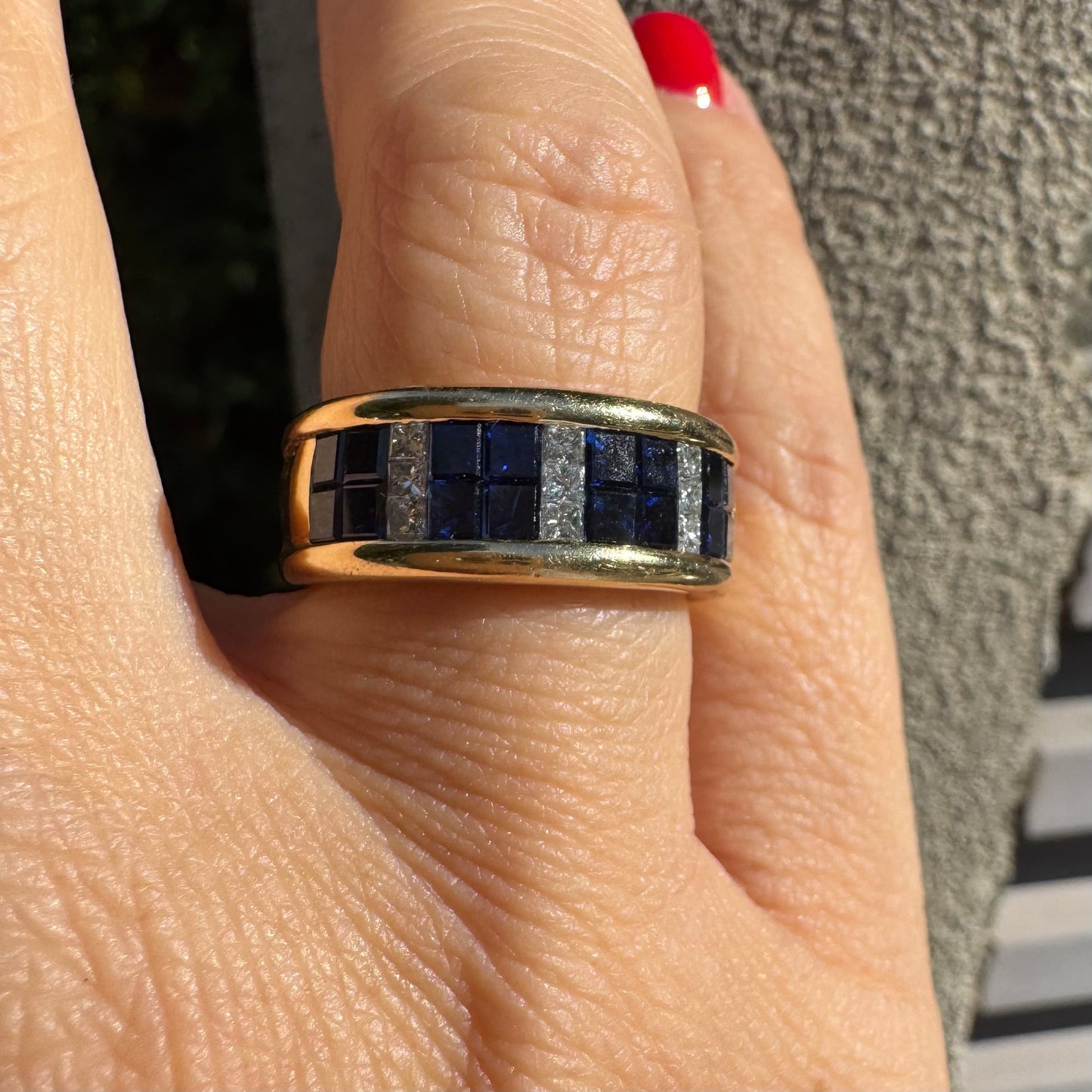 טבעת ה.שטרן זהב צהוב 18 קראט, בעיצוב רחב ומרשים. משובצת שורת אבני ספיר כחולות מרובעות בשילוב מחיצות של יהלומים לנגיעת ברק יוקרתי.