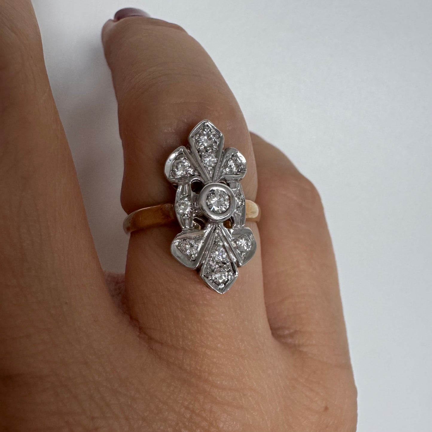 טבעת זהב לבן 14 קראט, בעיצוב אלגנטי ועדין, משובצת יהלום מרכזי עגול וסביבו יהלומים נוצצים נוספים.