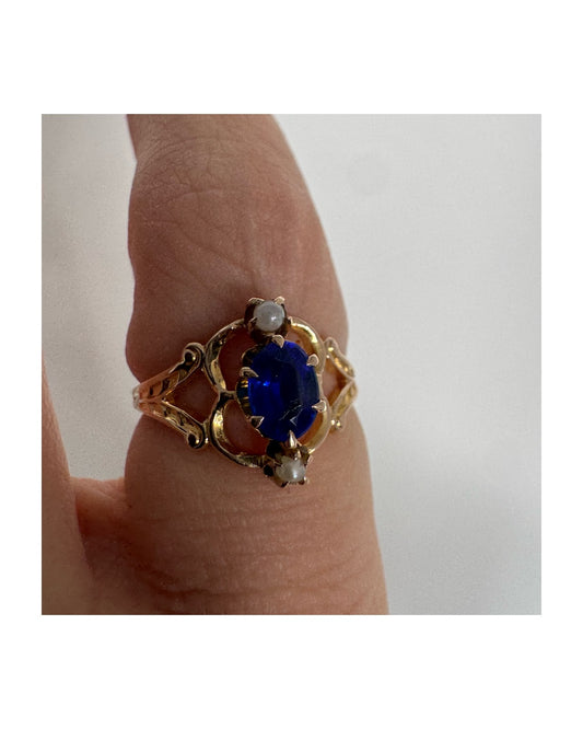 טבעת זהב צהוב 10 קראט משובצת אבן ספיר אובלית בגוון כחול עמוק ועשיר, ולצידה פנינים קטנות עדינות מעל ומתחת לאבן.