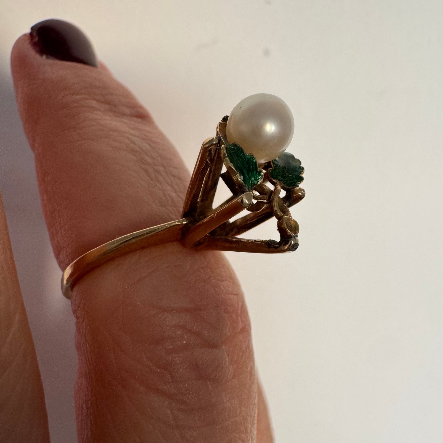 טבעת זהב 14 קראט משובצת פנינה מרכזית ומעוטרת אמייל ירוק בעבודת יד בצורת עלים.