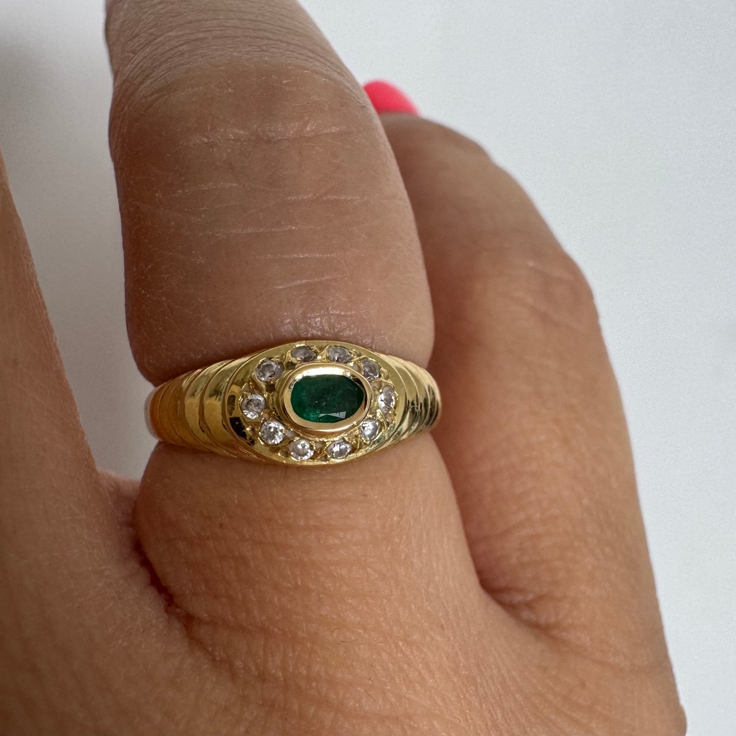 18K gold ring set with an oval Emerald at the center surrounded by Diamonds