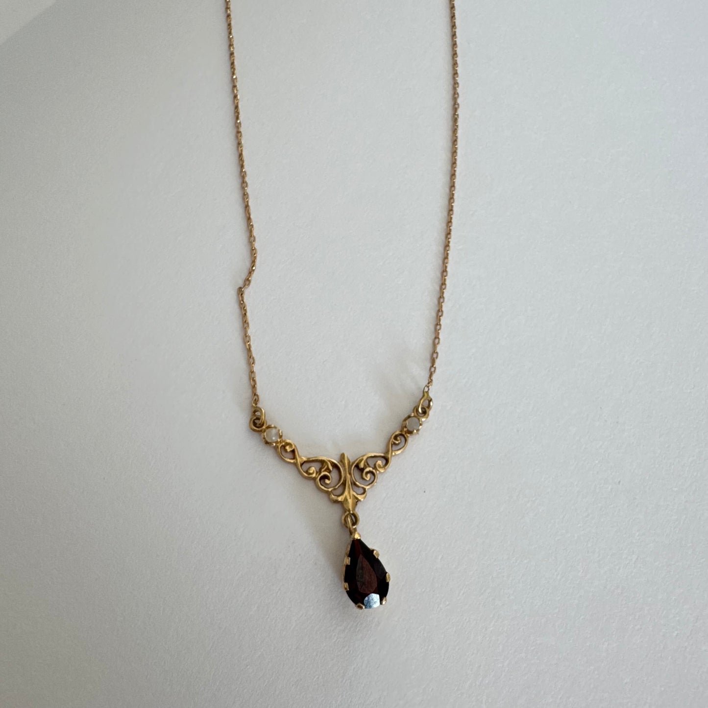 18K gold Necklace featuring an elegant scrollwork design and a striking deep-red pear-shaped Garnet drop.
