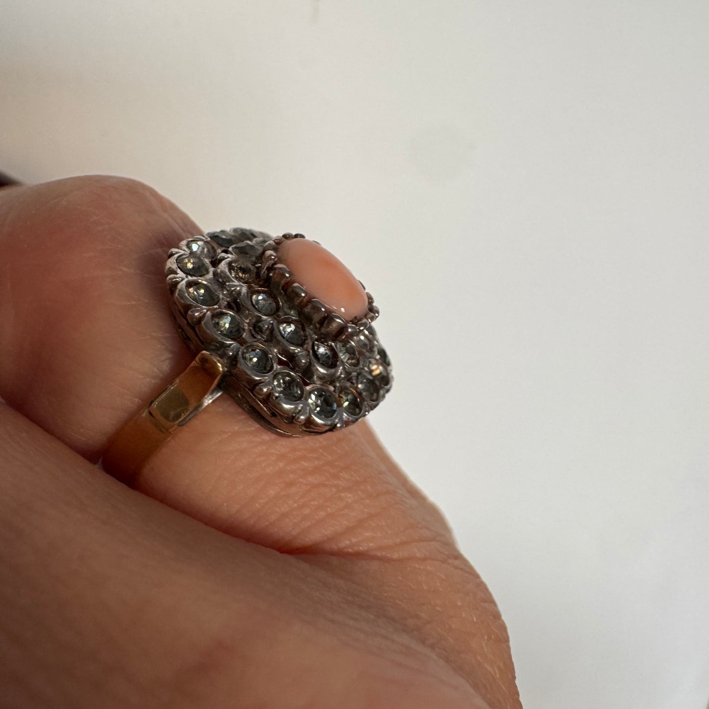 טבעת וינטג׳ עם חלק תחתון מזהב 14 קראט וחלק עליון עשוי כסף משובצת אבן קורל טבעית במרכז ומסביבה אבנים בהירות שאינן יהלומים.