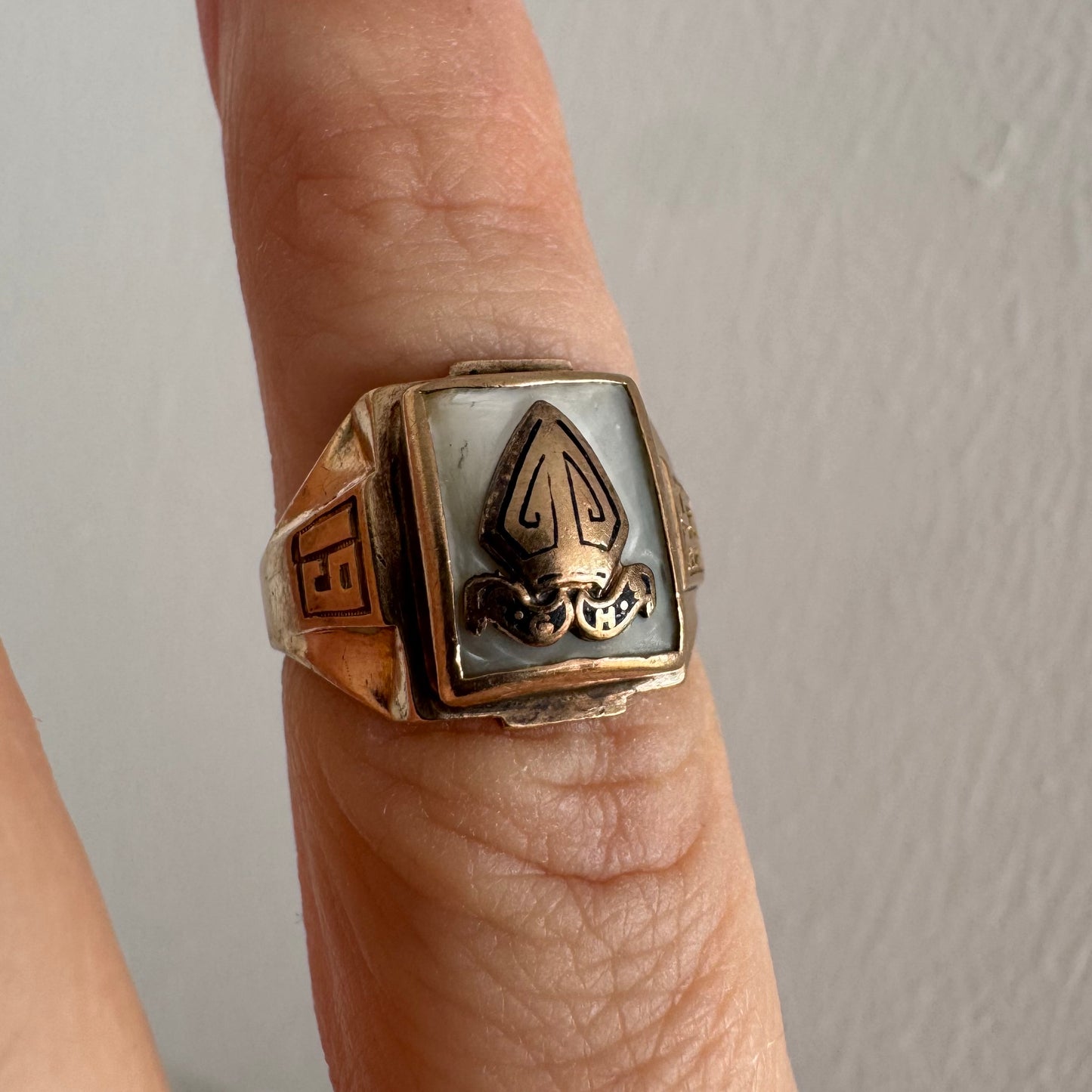 טבעת זהב 10 קראט בעיצוב חותם קלאסי, עם פלטה מרובעת משובצת לוח אם-הפנינה ועליה סמל פלר-דה-ליס מובלט.