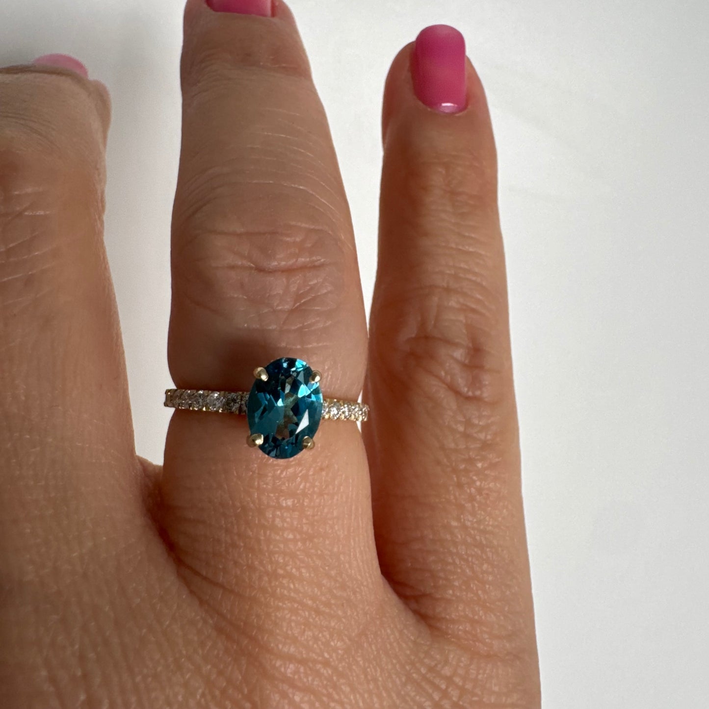 טבעת זהב צהוב 14 קראט משובצת אבן טופז כחולה אובלית בגוון טורקיז־כחול עמוק, באחיזה של ארבע שיניים עדינות ויהלומים.