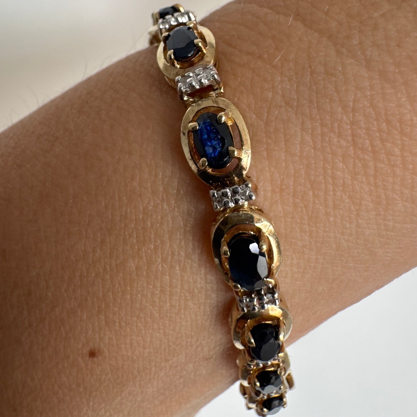 צמיד זהב צהוב 10 קראט בעיצוב קלאסי ועשיר, משובץ אבני ספיר אובליות בגוון כחול עמוק וביניהן שיבוצי יהלומים לבנים עדינים.