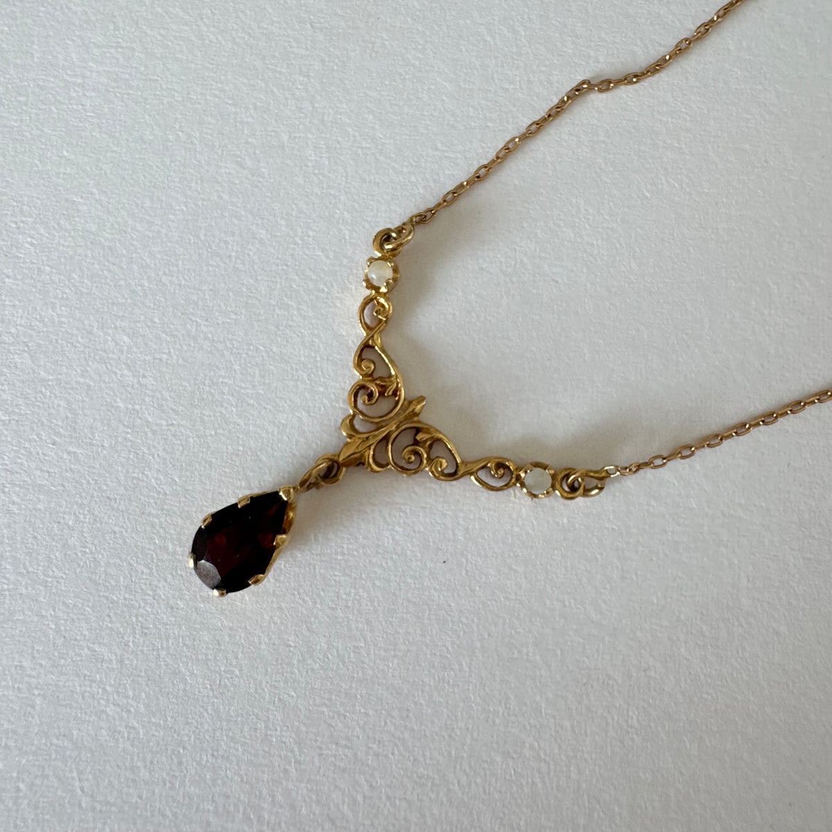 18K gold Necklace featuring an elegant scrollwork design and a striking deep-red pear-shaped Garnet drop.