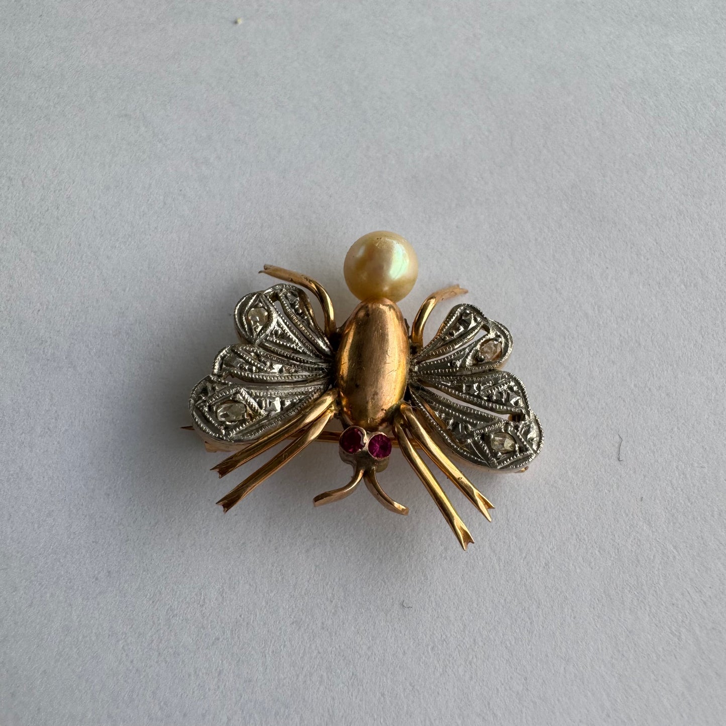 סיכת חרק ייחודית עשויה זהב 14 קראט משובצת יהלומים בעבודת פיליגרן עדינה בכנפיים, אבני רובי אדומות בעיניים ופנינה טבעית בגוון שמפניה.