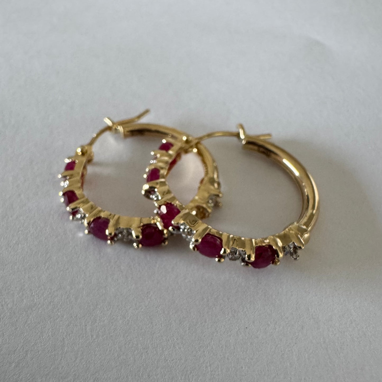 עגילי חישוק זהב צהוב 14 קראט משובצים אבני רובי בגוון אדום עמוק, בשילוב יהלומים המעניקים ברק עדין בין האבנים.