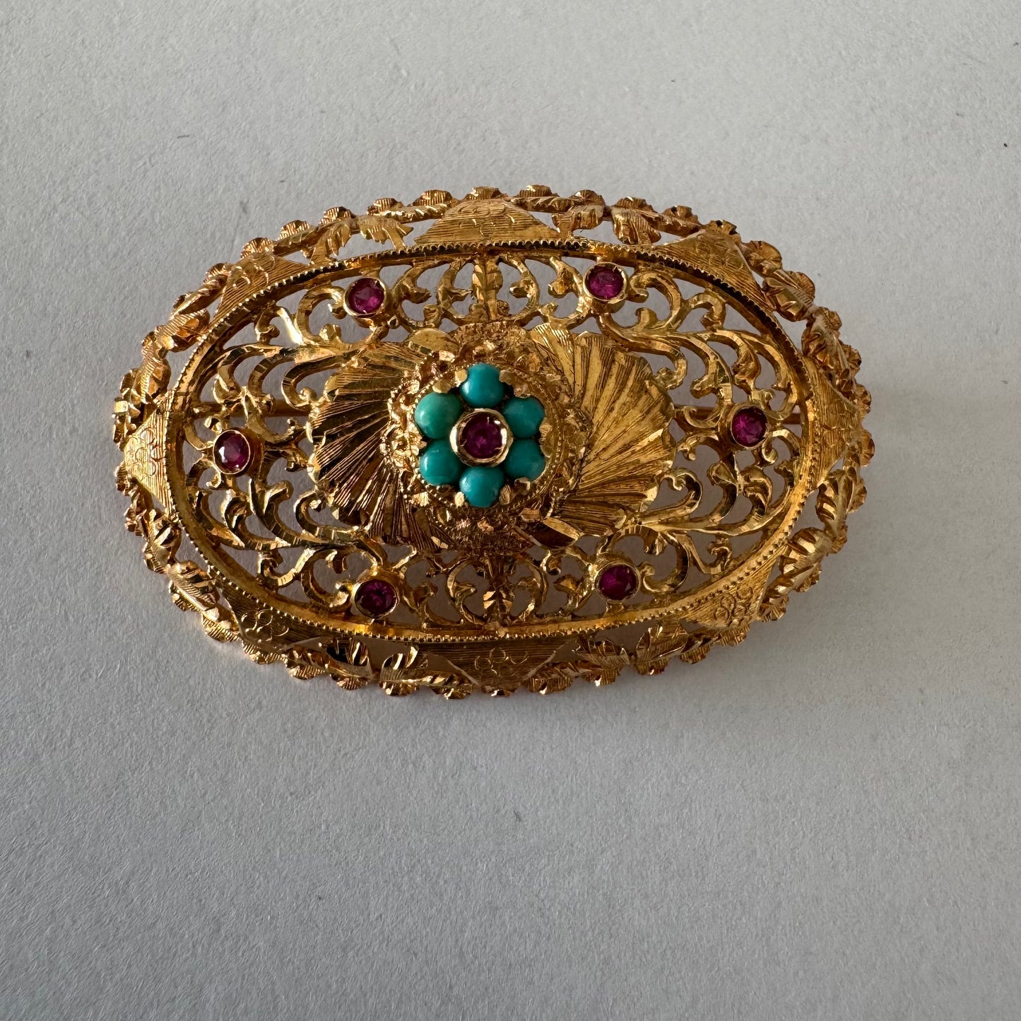 18K gold filigree brooch featuring intricate openwork detailing, accented with Ruby & Turquoise arranged in a floral centerpiece