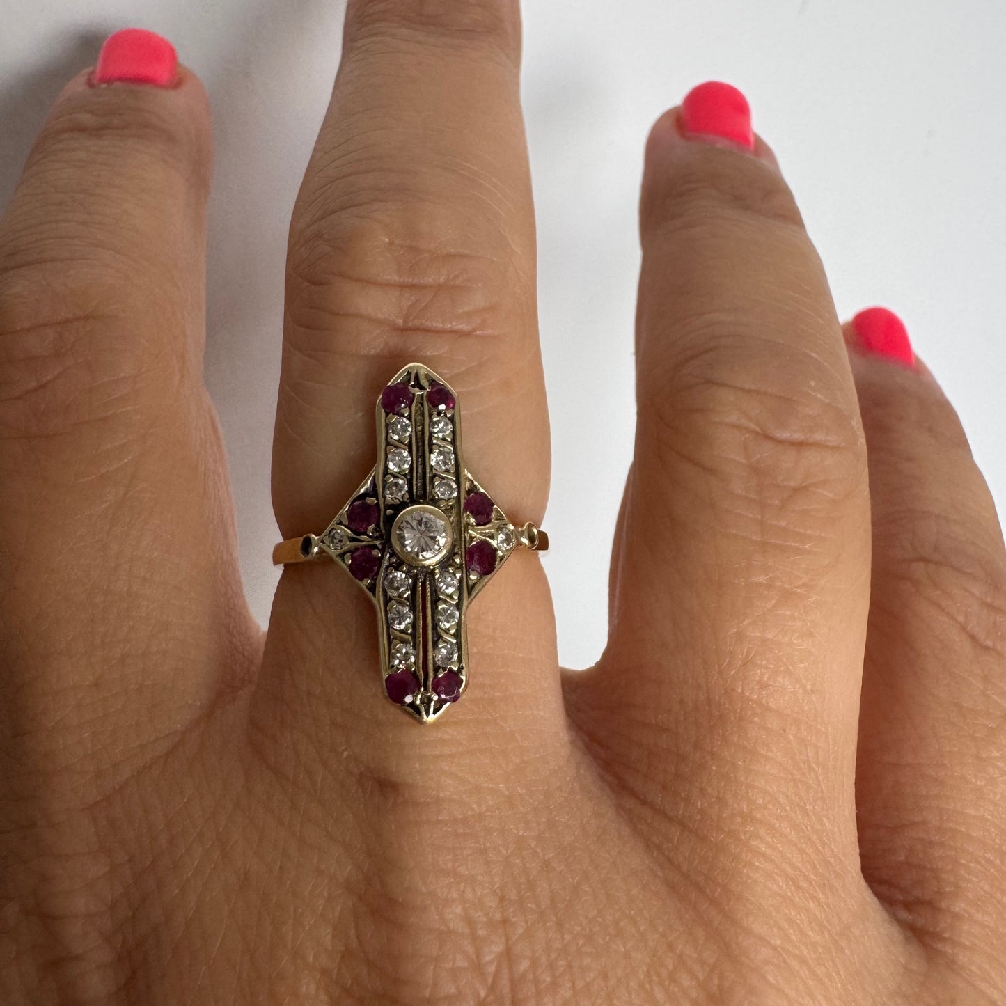 18K gold ring featuring a striking geometric design, set with a central Diamond surrounded by sparkling Diamonds and rich red Rubies.