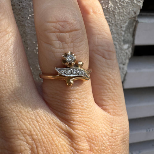 טבעת זהב אדום 14 קראט, עם שיבוץ בצורת פרח קטן ובו יהלום נוצץ לצד אלמנט מעוגל בצורת עלה משובץ יהלומים.