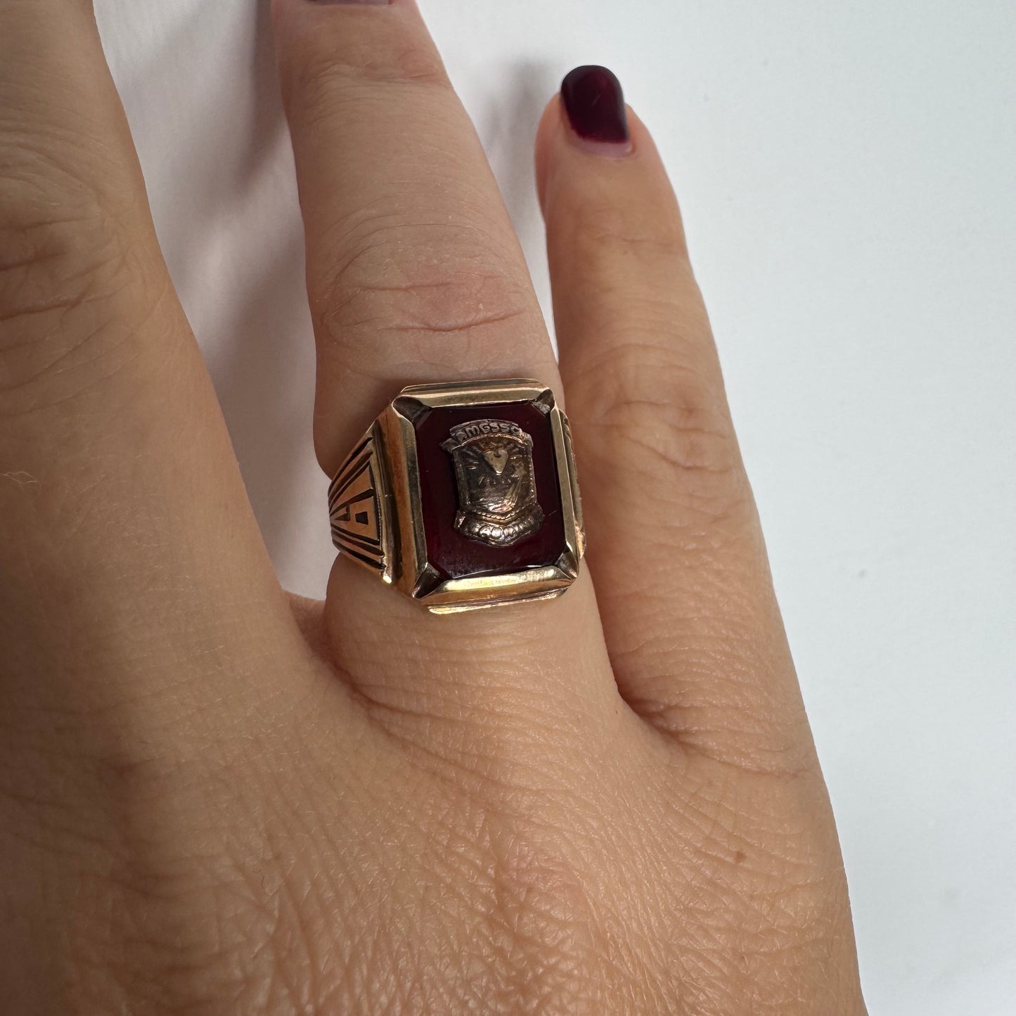 טבעת חותם זהב 10 קראט עם לוח מרכזי בגוון בורדו עמוק ועיטור סמל מובלט.