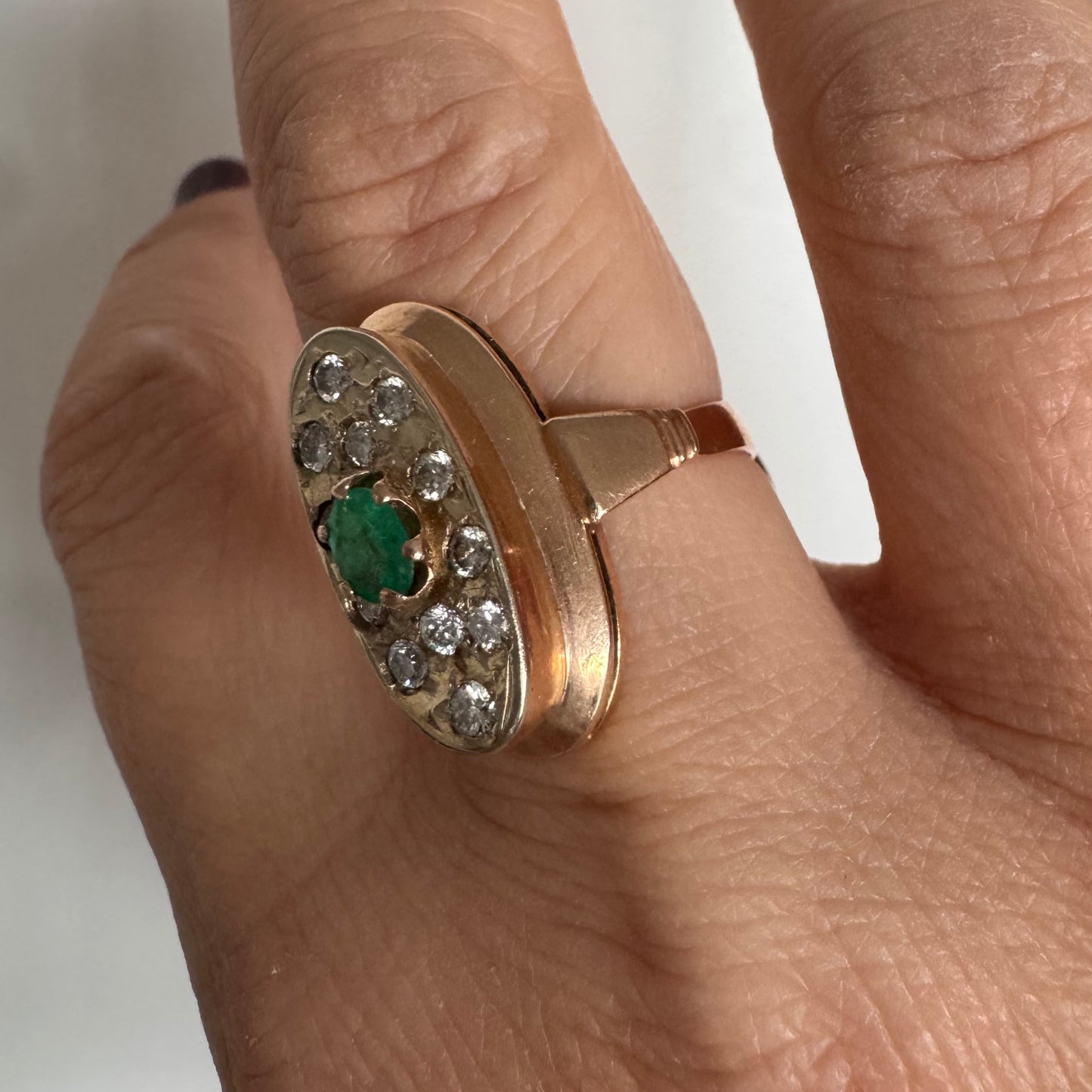 טבעת זהב 14 קראט בעיצוב אלגנטי ומאורך, משובצת אבן אמרלד מרכזית ויהלומים מסביב.