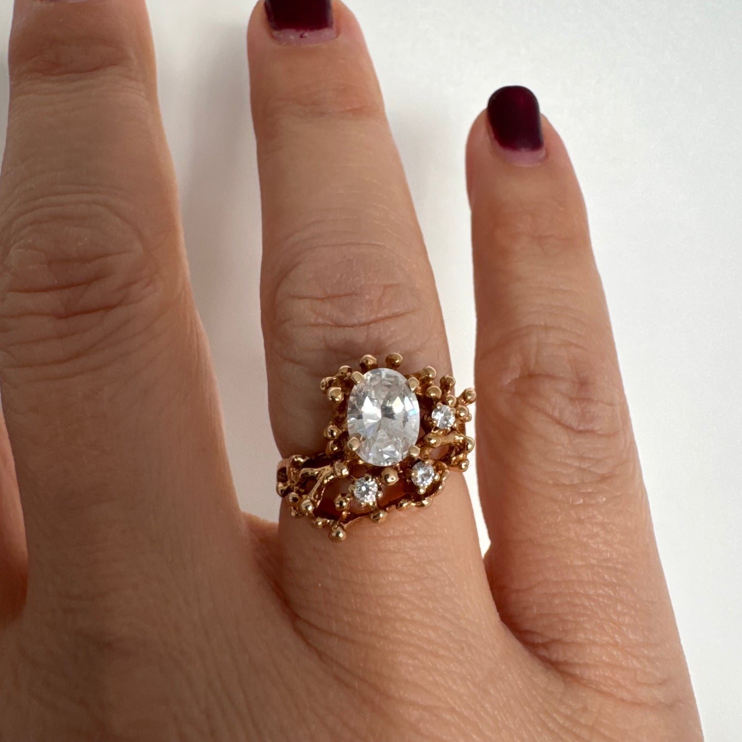 14K gold ring set with a central oval clear stone, accented by additional clear stones in an open, organic design.