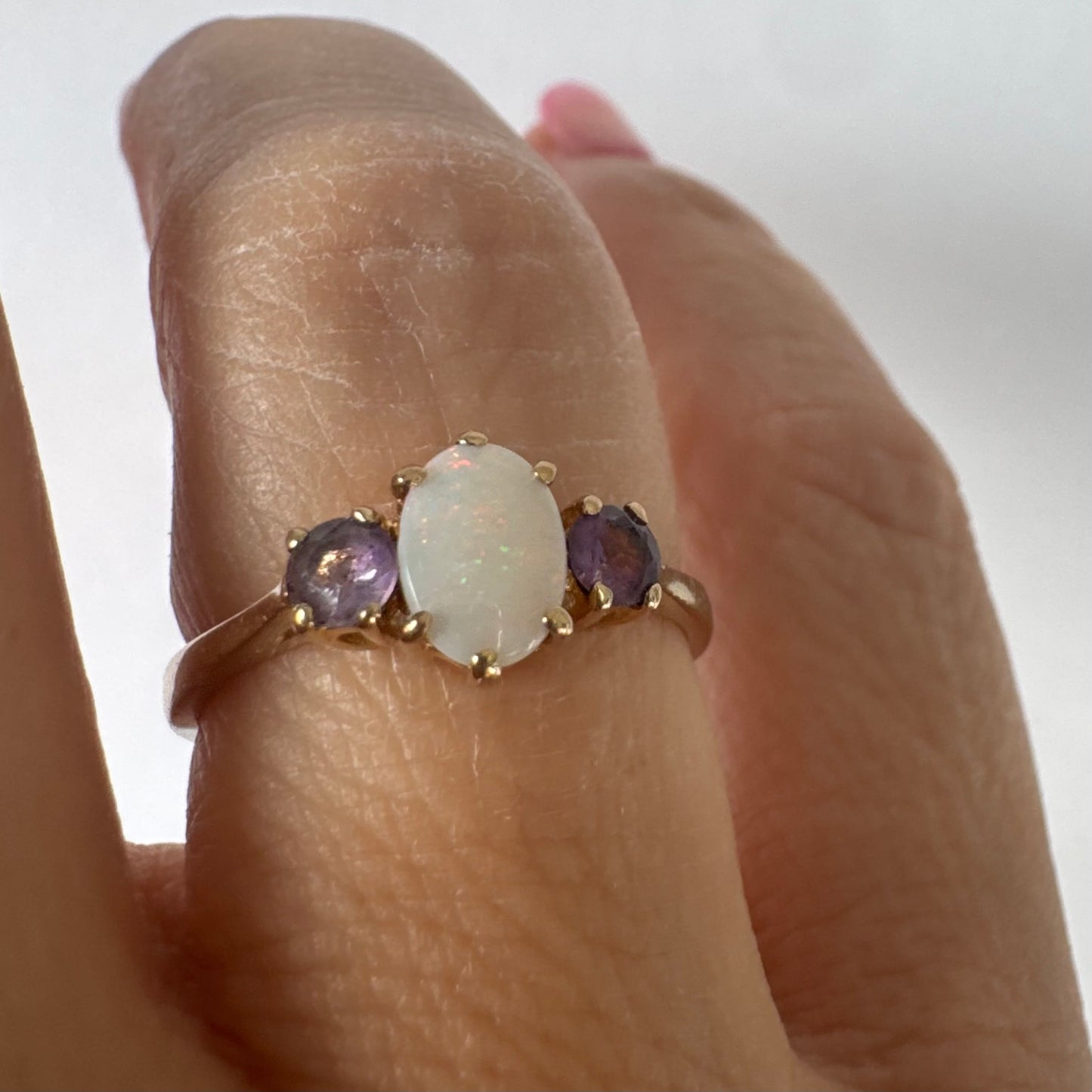 9K gold ring set with an oval Opal at the center, flanked by two delicate purple stones.