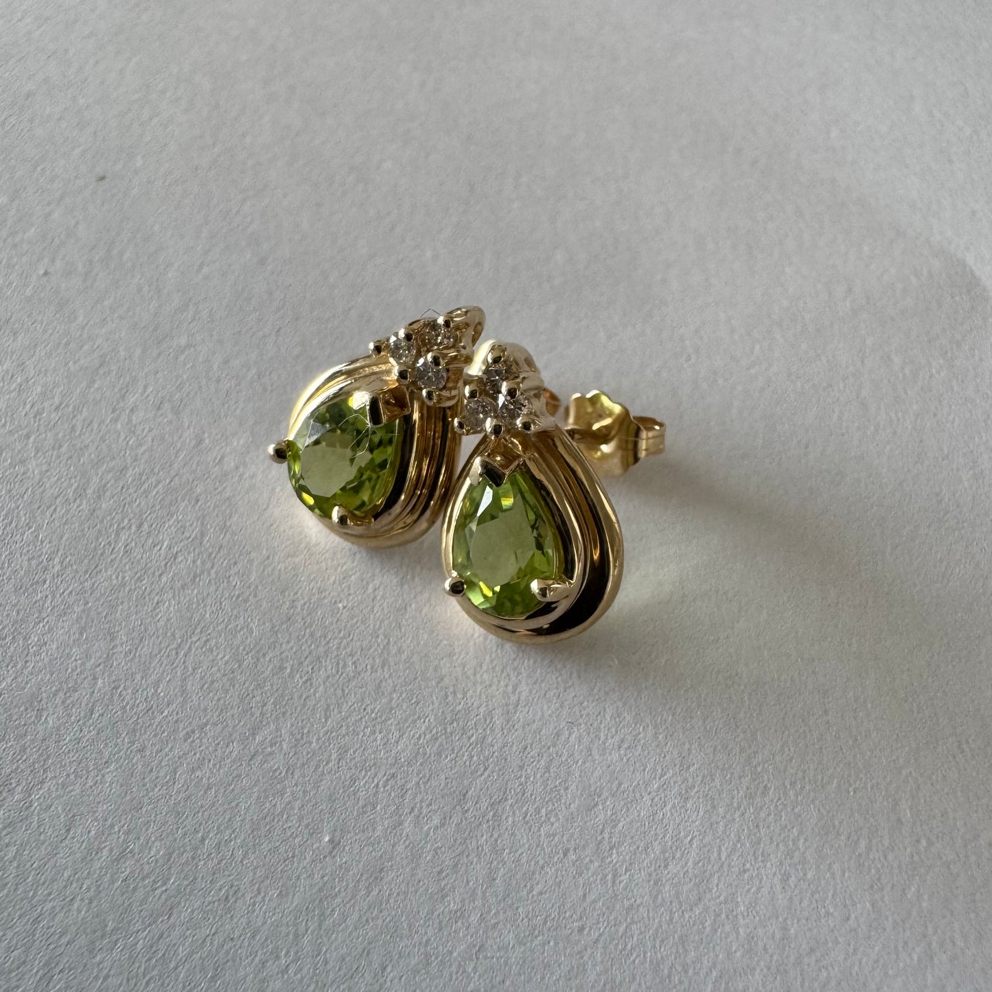 עגילי זהב צהוב 14 קראט משובצים אבני פרידוט בחיתוך טיפה, בגוון ירוק רענן ובוהק. 