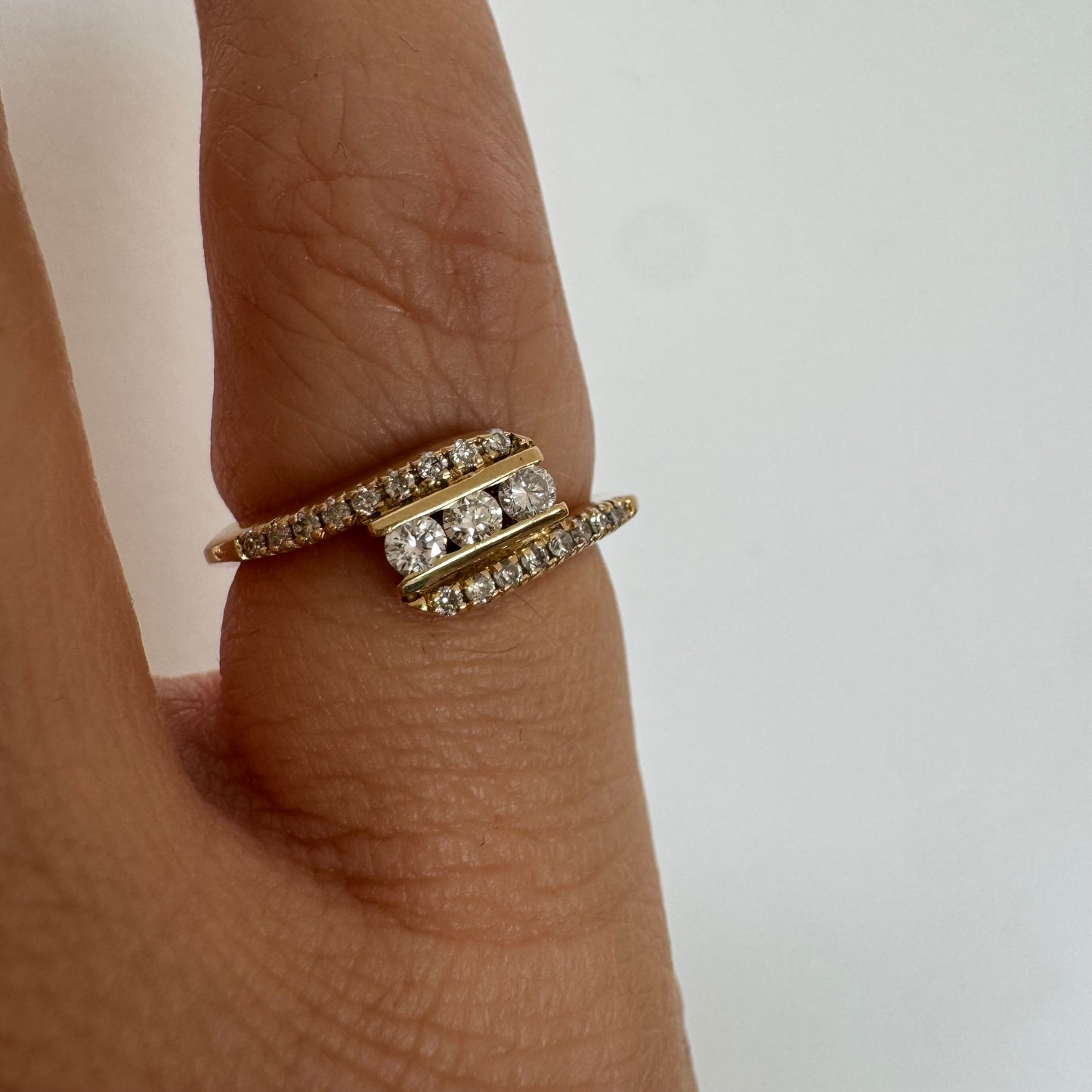 טבעת זהב צהוב 14 קראט בעיצוב ייחודי, משובצת שלושה יהלומים מרכזיים ושורות נוספות של יהלומים לאורך הזרועות. 