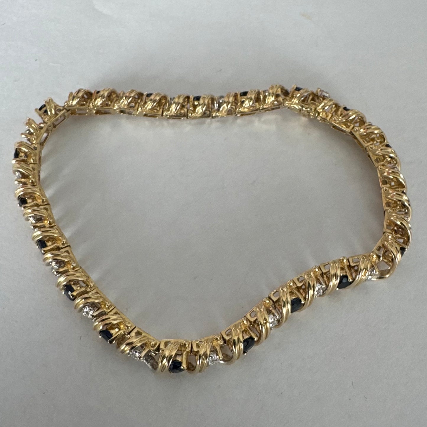 צמיד זהב צהוב 14 קראט משובץ אבני ספיר כחולות ויהלומים, המשובצים בעיצוב זורם עם קווים מעוגלים העוטפים כל אבן.