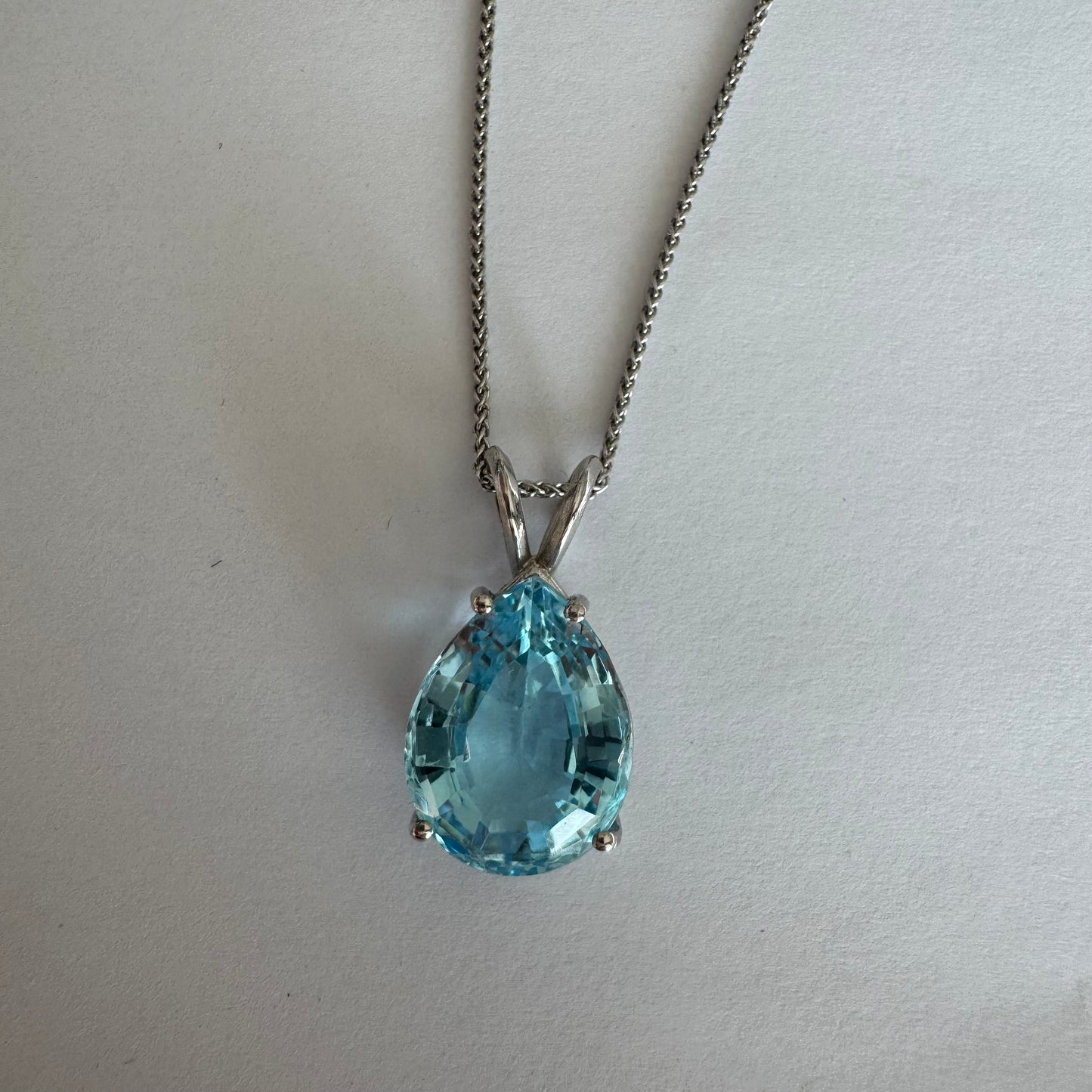 תליון זהב לבן 14 קראט המשובץ אבן טופז כחולה בחיתוך טיפה.