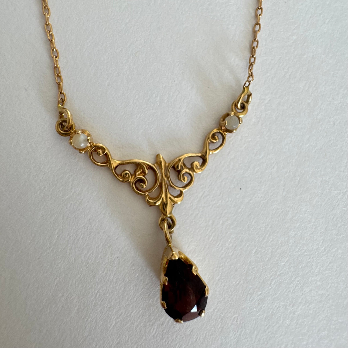 18K gold Necklace featuring an elegant scrollwork design and a striking deep-red pear-shaped Garnet drop.