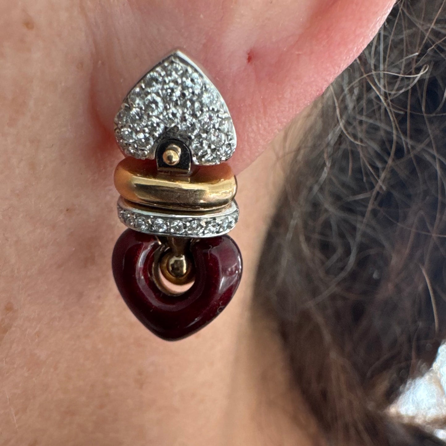 עגילי זהב 18 קראט בשילוב זהב צהוב ולבן, משובצים יהלומים בחלק העליון ובחישוק מרכזי, ובתחתית תליון לב אדום בגימור מבריק.