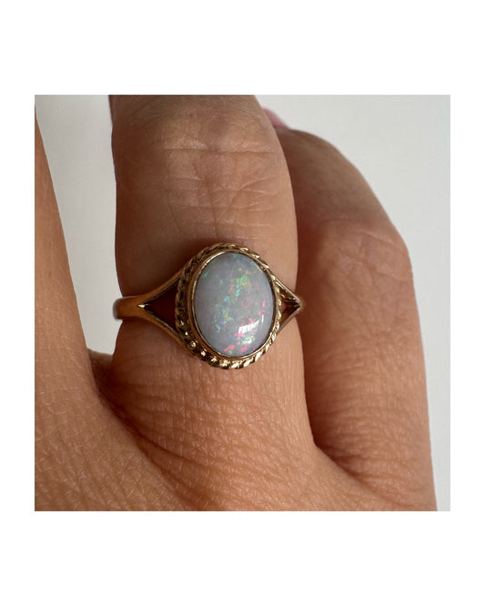 טבעת זהב צהוב 9 קראט משובצת אבן אופל אובלית עם משחק צבעים מרהיב של ירוק, ורוד וכחול.