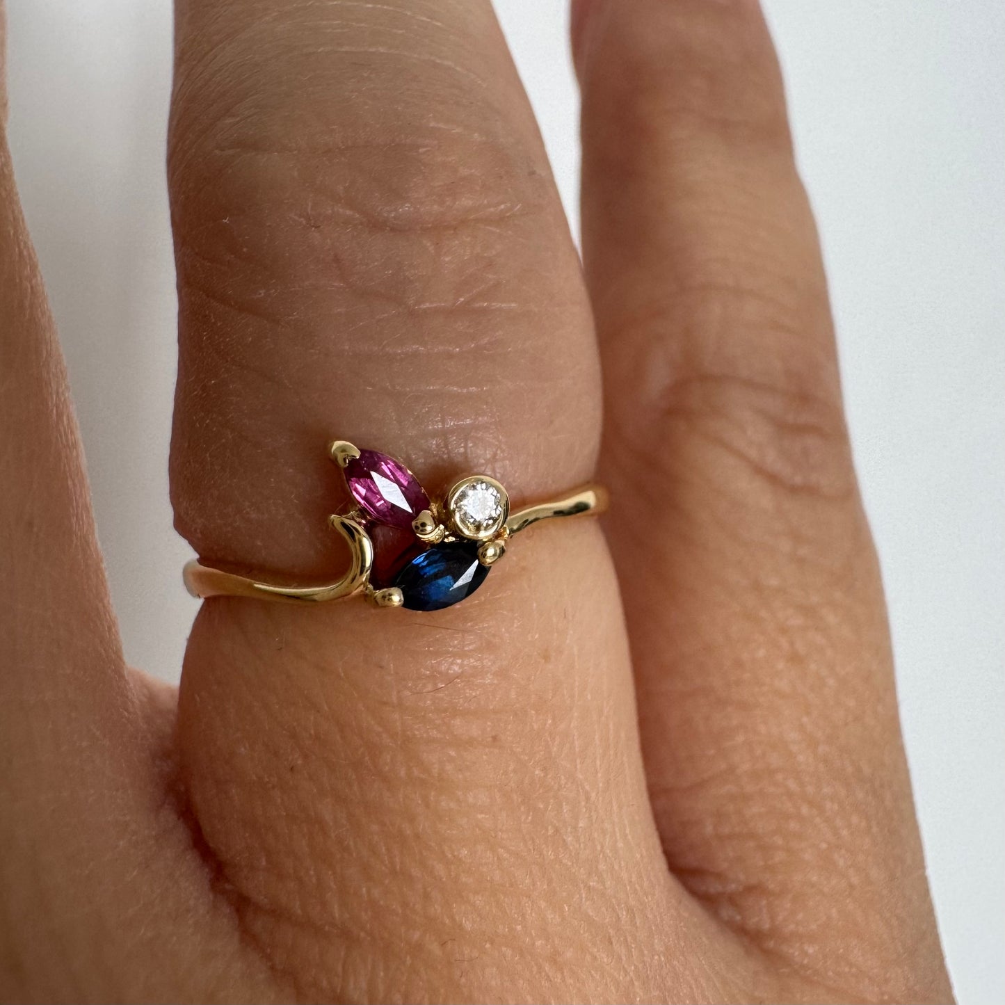 Delicate 18K gold ring set with pink and blue Sapphires alongside a sparkling center stone.