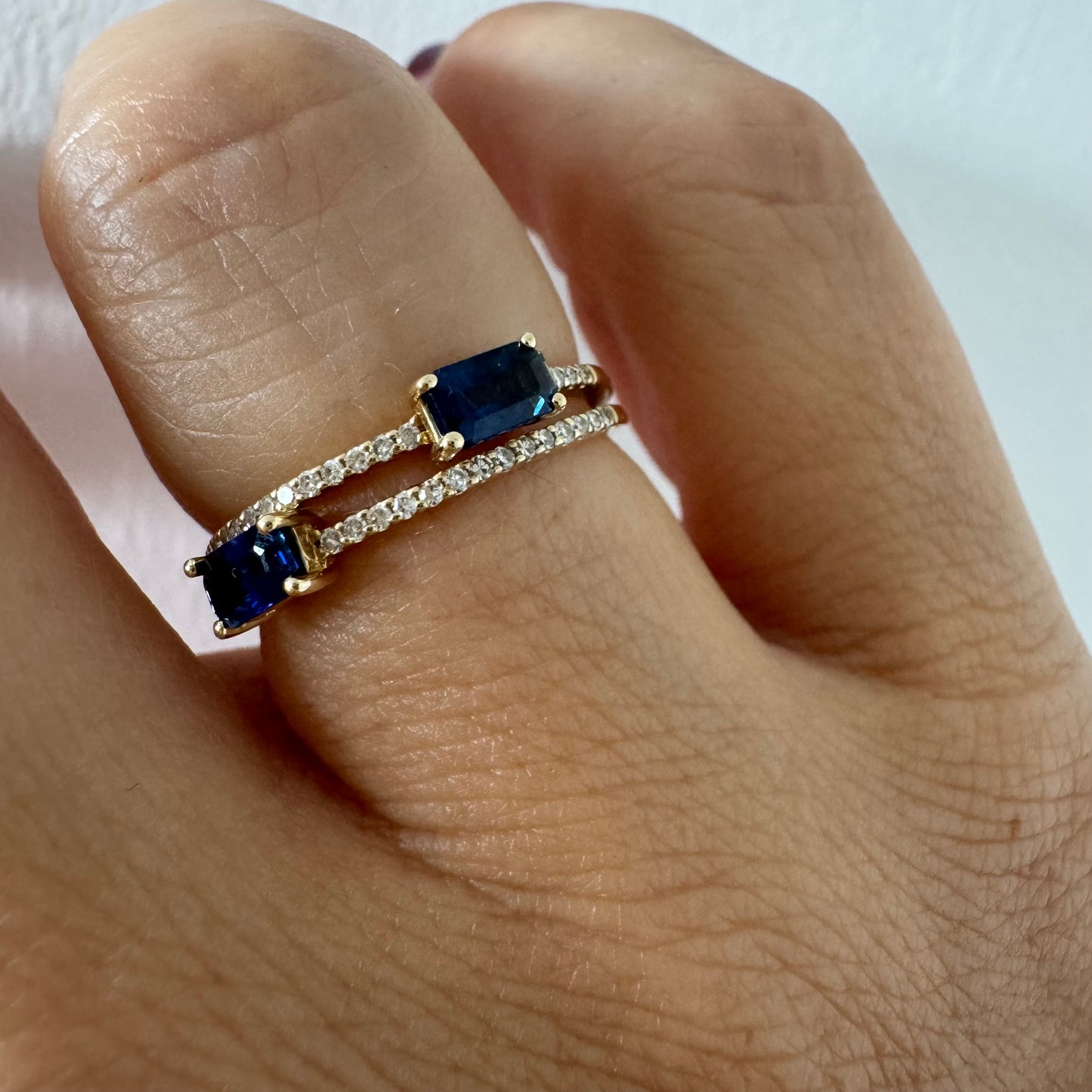 טבעת זהב צהוב 14 קראט בעיצוב פתוח, משובצת שתי אבני ספיר בחיתוך אמרלד ושורות יהלומים עדינים.