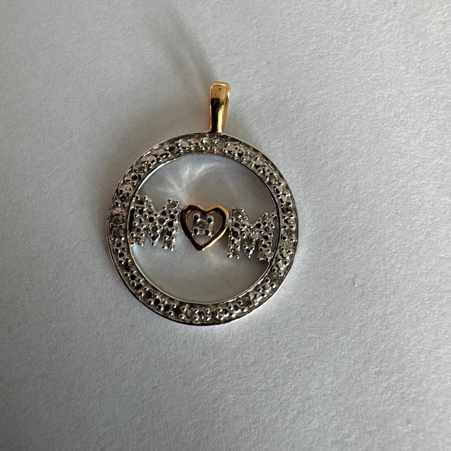 תליון זהב לבן 14 קראט עם הכיתוב ״MOM” מוקף מסגרת יהלומים עדינה.