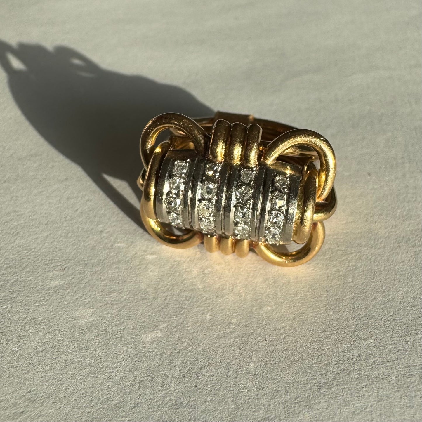 טבעת זהב צהוב ולבן 18 קראט עם מרכז בצורת חבית, משובצת יהלומים נוצצים.