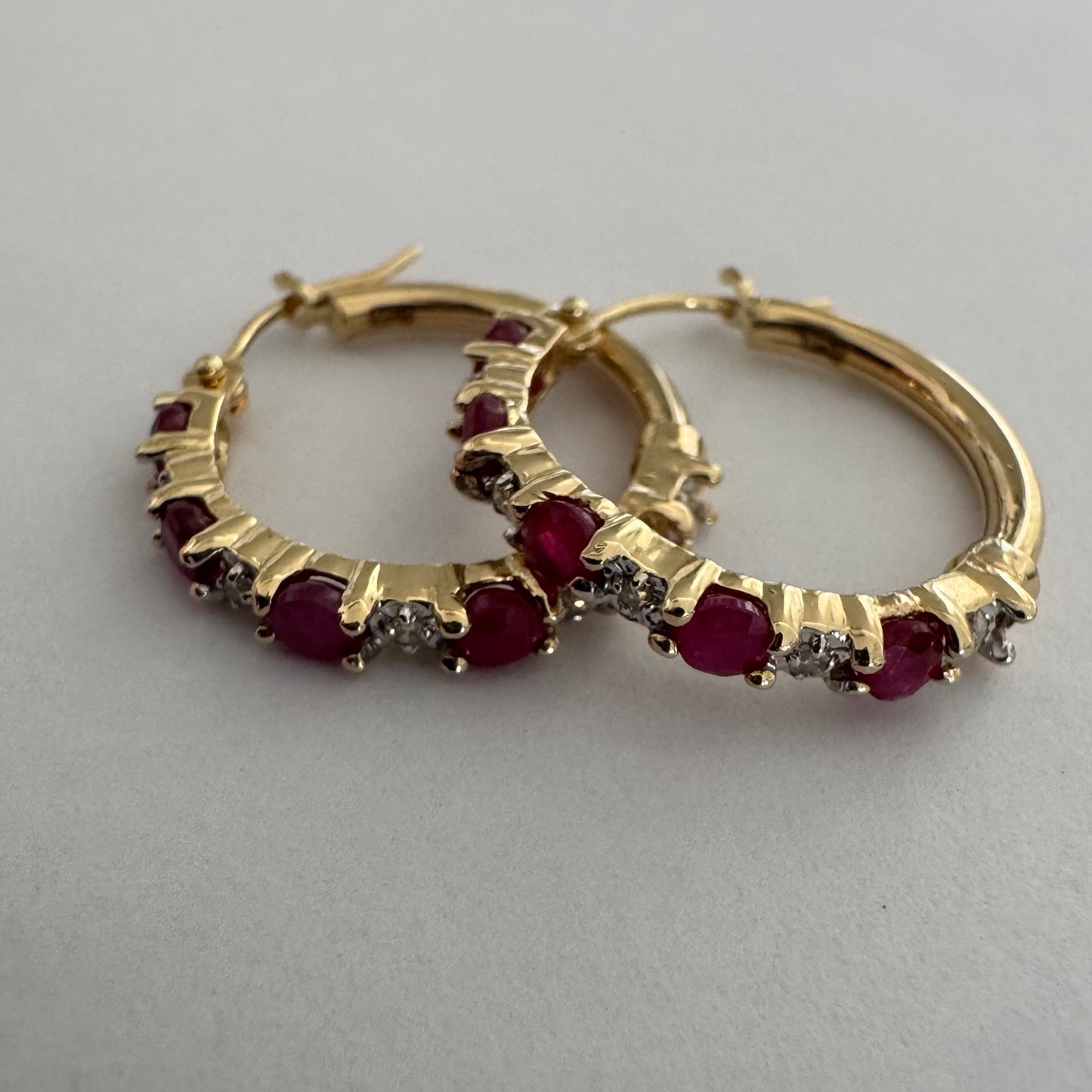 עגילי חישוק זהב צהוב 14 קראט משובצים אבני רובי בגוון אדום עמוק, בשילוב יהלומים המעניקים ברק עדין בין האבנים.