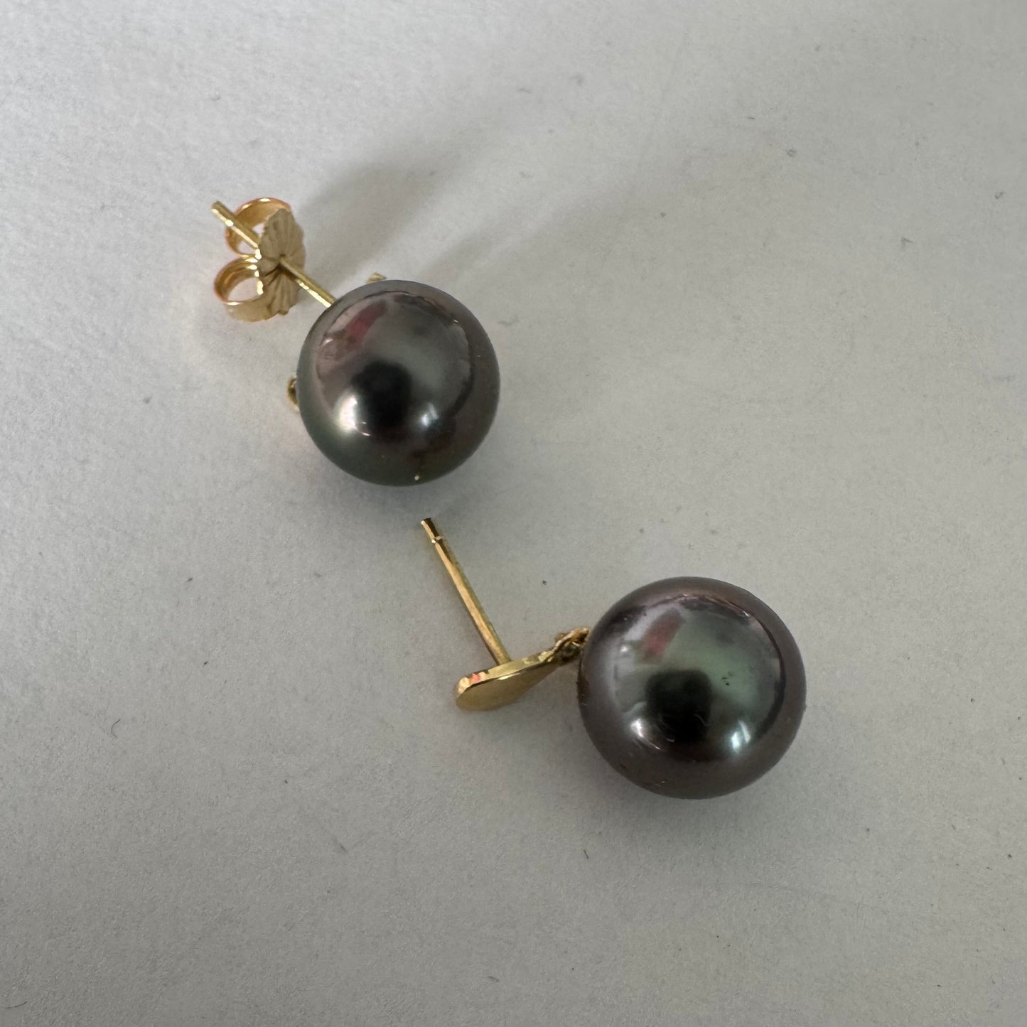 עגילי זהב צהוב 14 קראט משובצים פנינים עגולות בגוון כהה עם ברק עמוק ומשתנה.