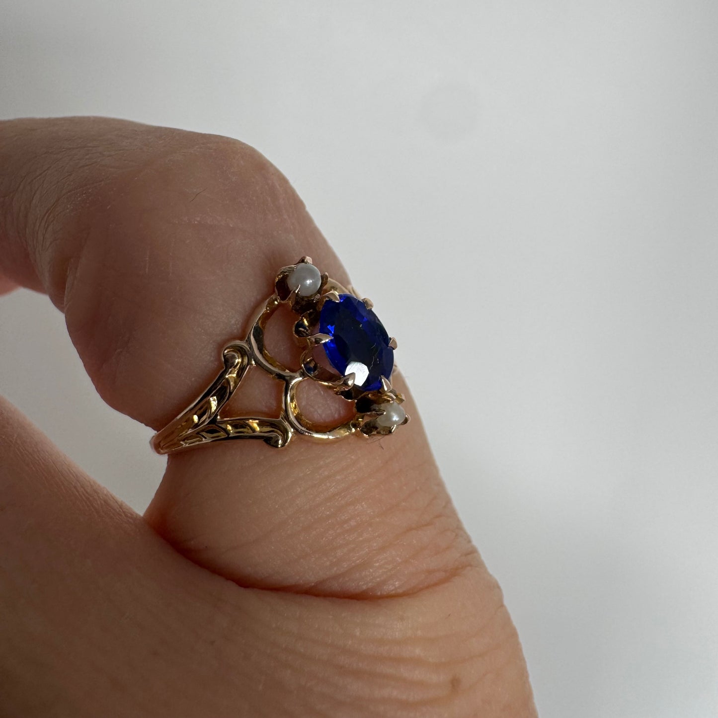 טבעת זהב צהוב 10 קראט משובצת אבן ספיר אובלית בגוון כחול עמוק ועשיר, ולצידה פנינים קטנות עדינות מעל ומתחת לאבן.