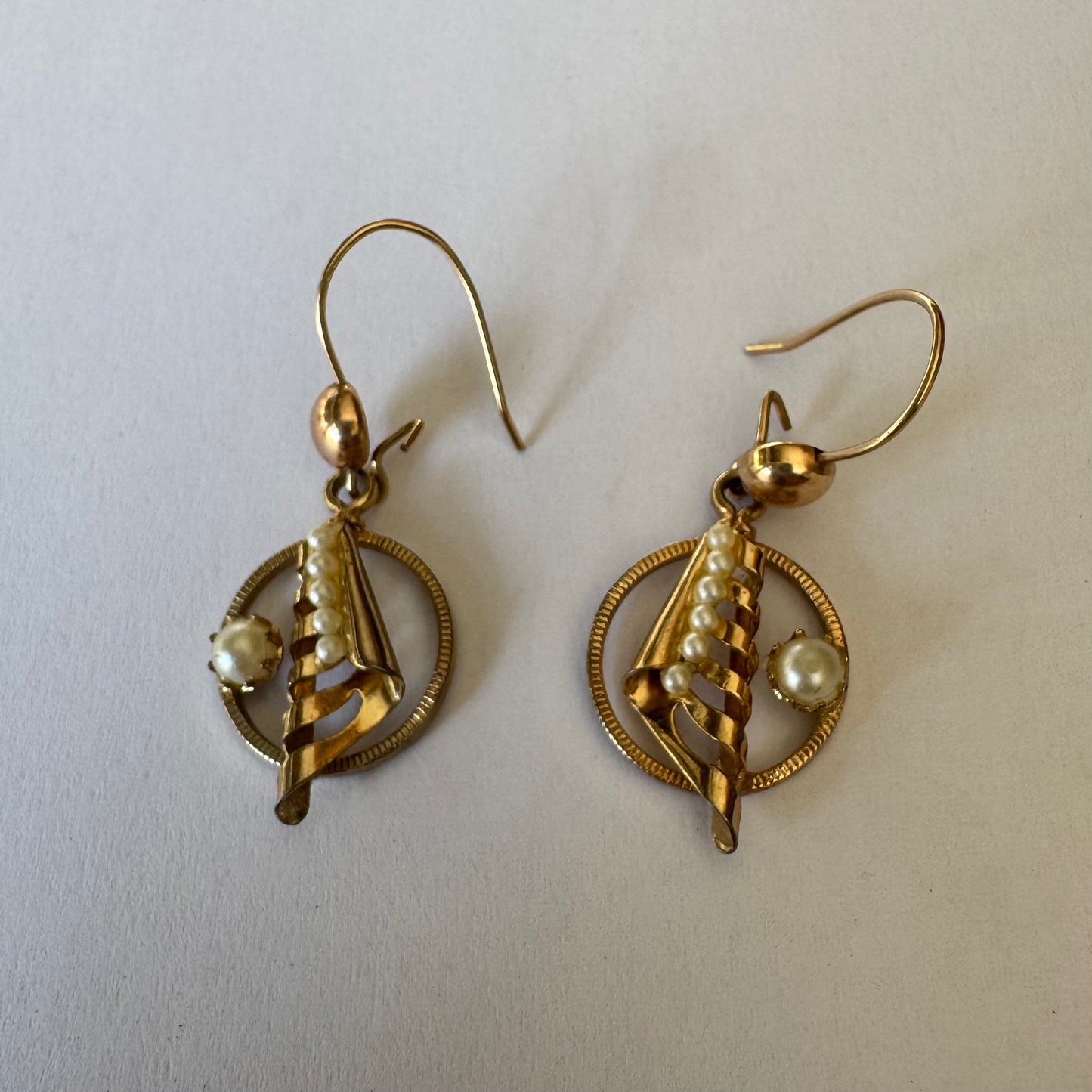 עגילי זהב 10 קראט, בעיצוב עדין עם אלמנט ספירלי ושילוב פנינים קטנות בגוון לבן-קרם. 