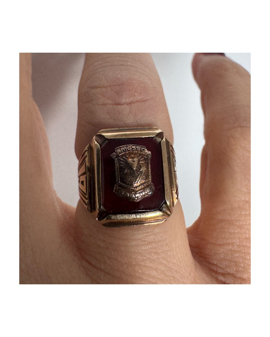 טבעת חותם זהב 10 קראט עם לוח מרכזי בגוון בורדו עמוק ועיטור סמל מובלט.