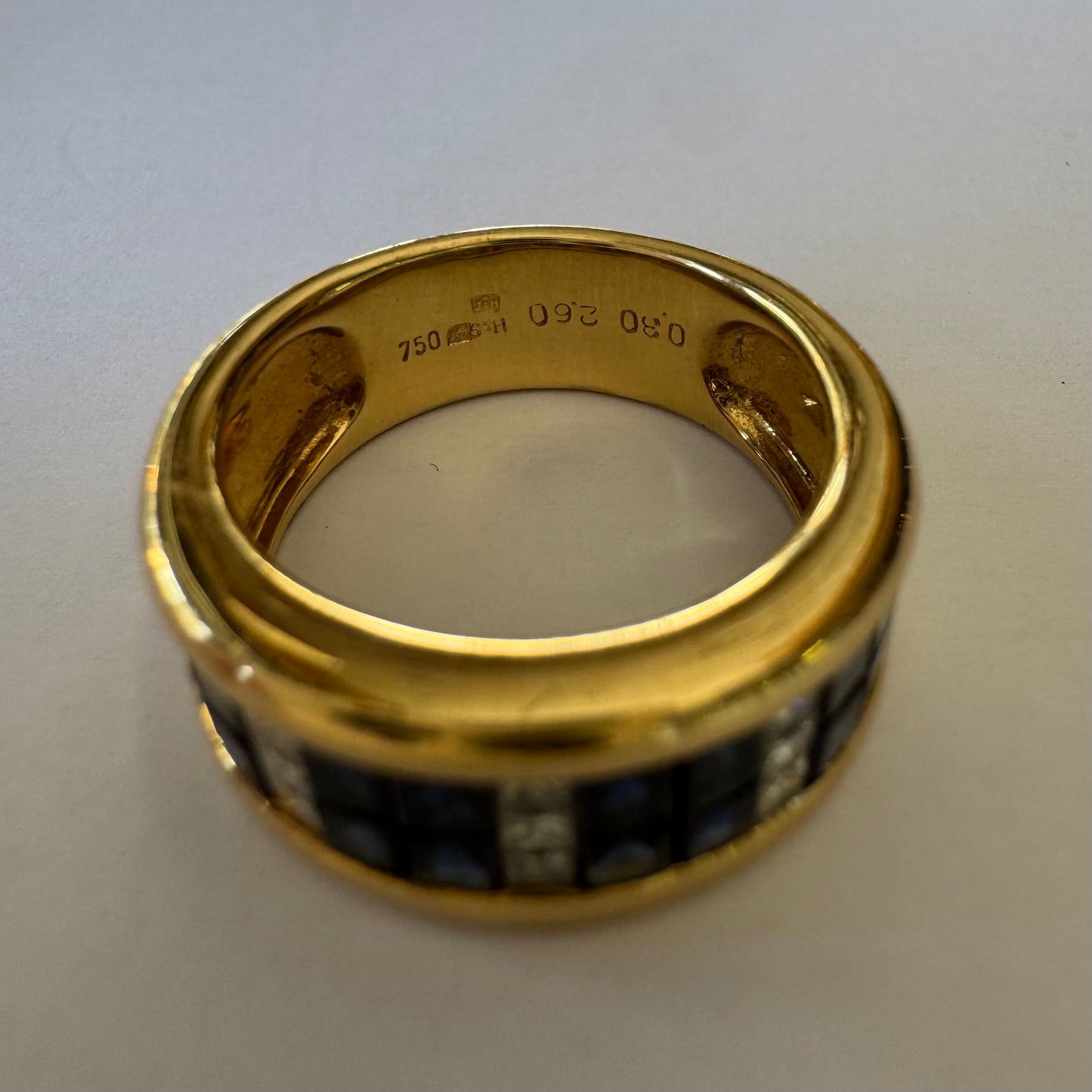 טבעת ה.שטרן זהב צהוב 18 קראט, בעיצוב רחב ומרשים. משובצת שורת אבני ספיר כחולות מרובעות בשילוב מחיצות של יהלומים לנגיעת ברק יוקרתי.