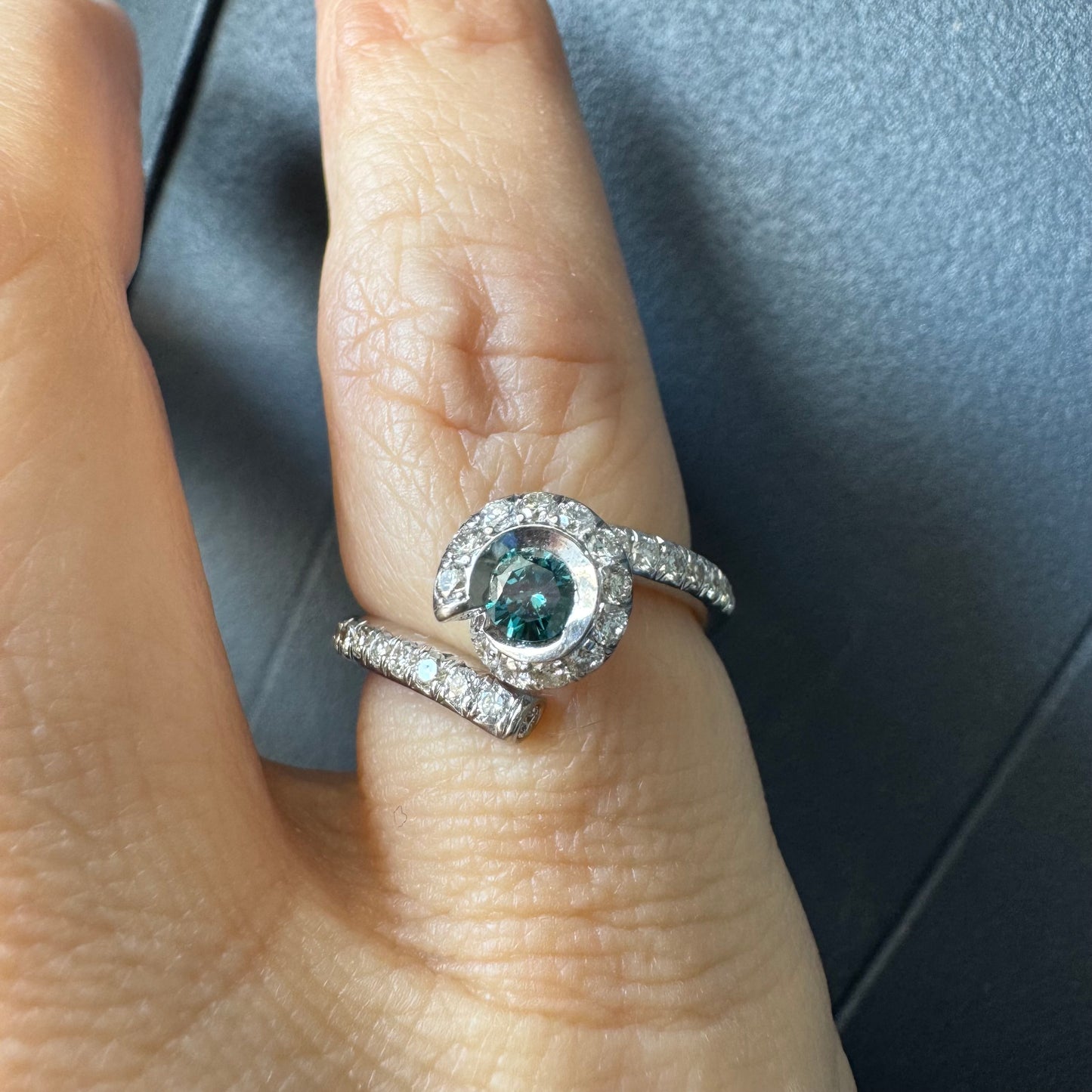 טבעת זהב לבן 18 במרכזה משובץ יהלום כחול עז, מוקף בהילה של יהלומים לבנים והזרועות של הטבעת משובצות יהלומים